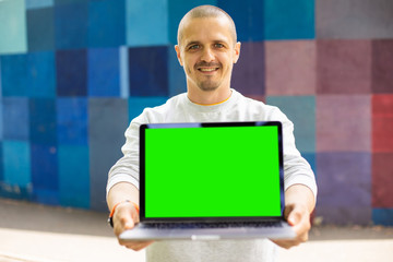 Smiling man looking in camera and holding laptop with chromakey green screen