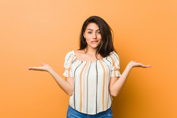 Young curvy woman confused and doubtful shrugging shoulders to hold a copy space.