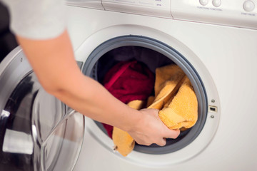 Loading clothes in washing machine. Housework and laundry concept