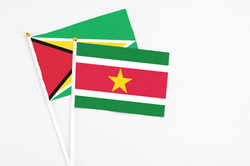 Suriname and Guyana stick flags on white background. High quality fabric, miniature national flag. Peaceful global concept.White floor for copy space.