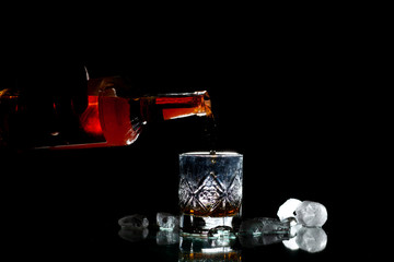 barman pours whiskey into a glass with ice on a black background, his hand holds a bottle of rum