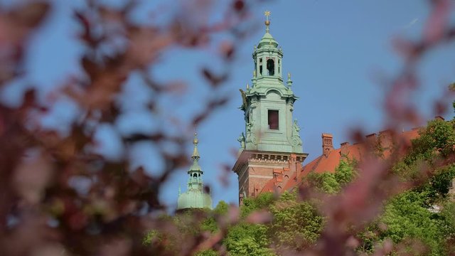 View through trees of a medieval church cathedral tower inside the walls of Wawel castle in Krakow, Poland.