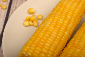 Two ears of boiled corn in a plate and a grain of corn on the table. Healthy diet. Fitness diet. For a sweet treat. Close up.
