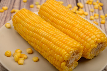 Two ears of boiled corn in a plate and a grain of corn on the table. Healthy diet. Fitness diet. For a sweet treat. Close up.