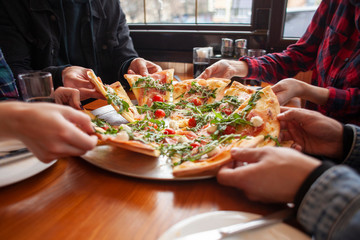 group of students friends eat Italian pizza, hands take slices of pizza in a restaurant