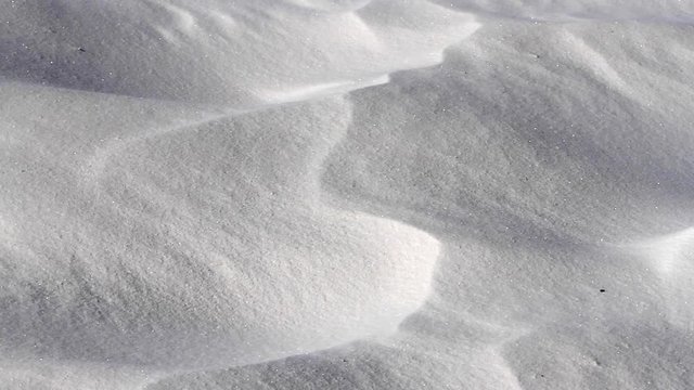 White sand being blown over the tiny ridges of a large desert sand dune.