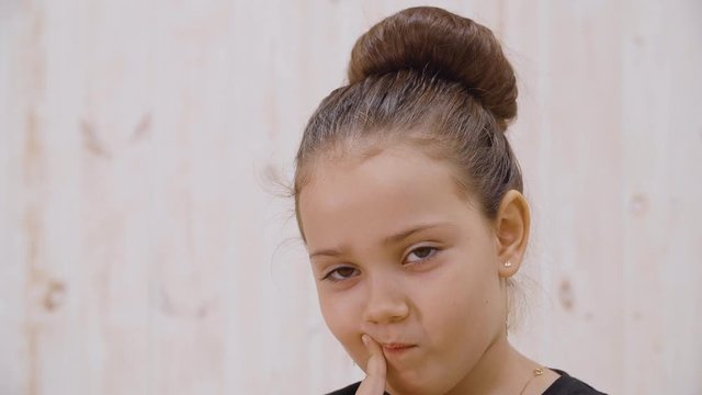 Close-up view of cute thoughtful little girl looking at camera. Portrait of adorable pensive preteen girl with finger on face looking up and looking at camera