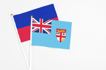 Fototapeta premium Fiji and Haiti stick flags on white background. High quality fabric, miniature national flag. Peaceful global concept.White floor for copy space.
