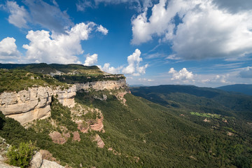 Fototapeta na wymiar High rock with blue sky and white clouds. Green forest at the bottom of the valley, Tavertet, Catalonia.