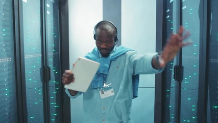 Ecstatic happy african engineer dancing in server corridor having fun flirting playing at camera with excitement. Smart handsome dancer in data center. - Powered by Adobe