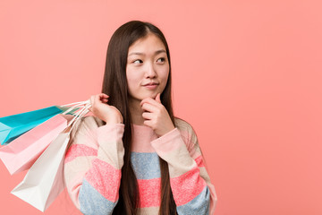 Young asian woman holding a shopping bag looking sideways with doubtful and skeptical expression.