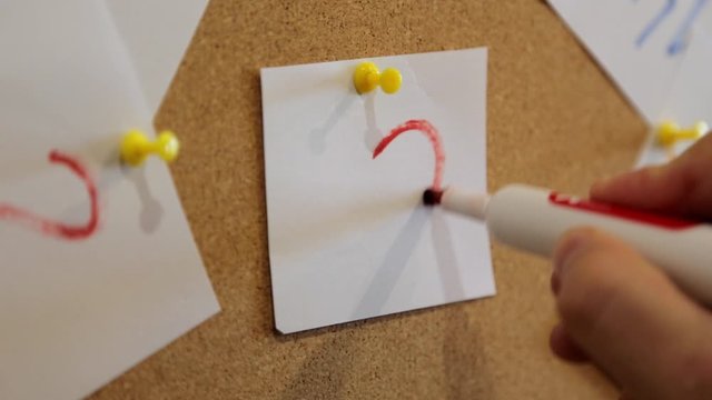 Love concept. A man with a red marker draws a heart on a white sheet of paper, which is attached with a red pin to a cork board.