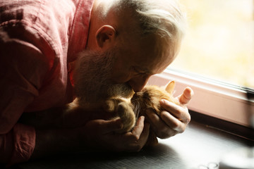 Senior man holding cute red cat at home. Man and cat hugging. 