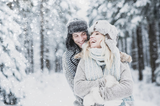 young, pretty, in love couple with winter cap and scarf in the winter forest hug each other and have fun together