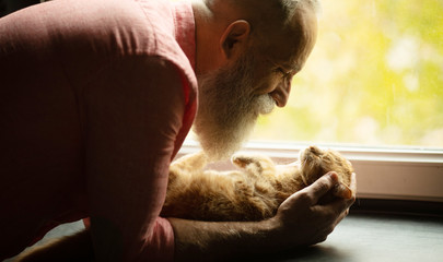Senior man holding cute red cat at home. Man and cat hugging. 