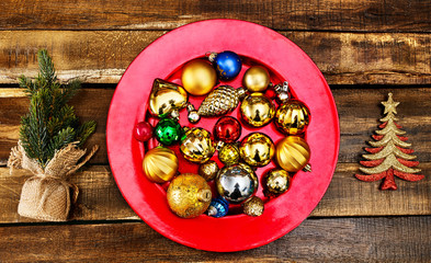 Christmas decorations design of Xmas balls ornaments on red plate with green tree on wooden boards. Horizontal frame
