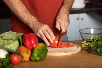 Chef's hands cutting red fresh tomato on a wooden board.