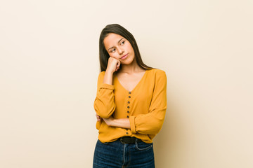 Young hispanic woman against a beige background who feels sad and pensive, looking at copy space.