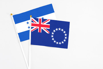 Fototapeta premium Cook Islands and Honduras stick flags on white background. High quality fabric, miniature national flag. Peaceful global concept.White floor for copy space.