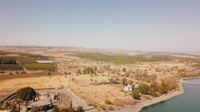 Aeral dolly over Lake Capernaum, shore view, Orthodox Church of the 12 apostles. The coast of Sea of Galilee, top view of the hills, green fields and the road.