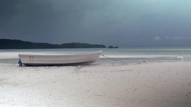 close up of a small boat on a white beach and dark monsoon storm looms in background