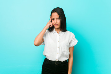 Young hispanic cool woman against a blue wall pointing temple with finger, thinking, focused on a...