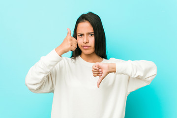 Young pretty hispanic woman showing thumbs up and thumbs down, difficult choose concept