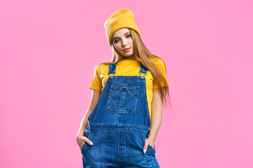 Portret a pretty girl in denim overalls and a yellow hat on a pink background. Fashionista lady student smiling . Bright trendy studio fashion image of sexy model, wearing neon bright color block © Aleksandr Rybalko