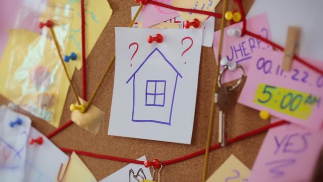 Real Estate search concept. Close-up view of a detective board with evidence. In the center Woman's hand pins a white sheet of paper with the house icon