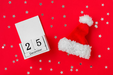 Santa Claus red hat and white wooden perpetual calendar with date 25 december on a red background with silver stars. Festive flat lay for Christmas and New Year greeting card.
