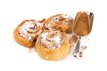 three home made cinnamon buns with white frosting with a scoop of cinanamon isolated on white