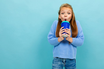 teenager girl happily drinks through a straw from a glass on a blue background