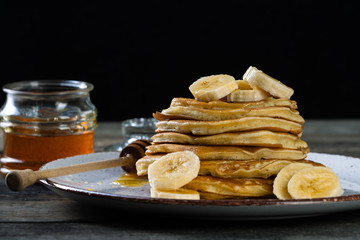pancakes lie on a plate poured with honey with a honey spoon and decorated with bananas. plate with pancakes on an old wooden background  with place for inscription