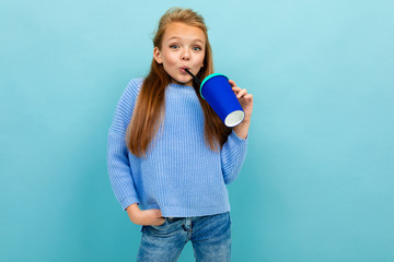 beautiful fashionable girl drinks from a paper cup on a background of blue wall