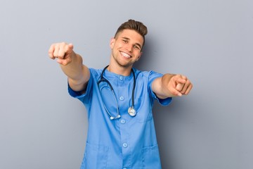 Young nurse man cheerful smiles pointing to front. - obrazy, fototapety, plakaty