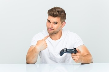 Young man holding a game controller pointing with finger at you as if inviting come closer. © Asier