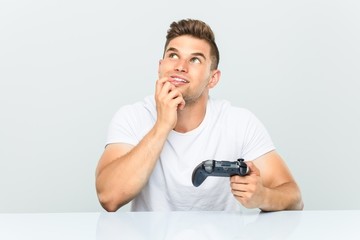 Young man holding a game controller relaxed thinking about something looking at a copy space. © Asier