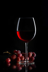 Glass of red wine and bunch of grapes on the dark background