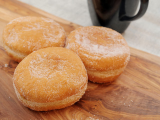 Three fresh tasty doughnuts with sugar coating on a wooden board and black tea cup. Close up.