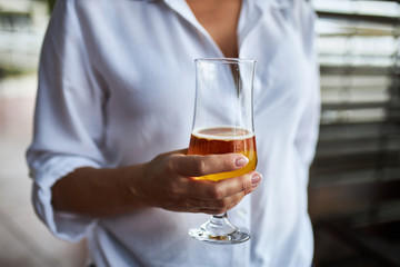 Glass of tasty light beer in the hand of a young woman