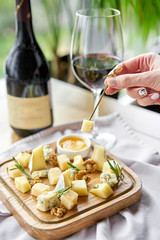 Girl holding piece of parmesan cheese on a skewer and wooden plate with cheese. Delicious cheese mix with walnuts, honey. Food for wine.