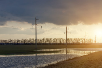 Obraz premium Power line along the road and green field with large puddles after rain in early spring