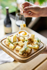 Girl holding piece of parmesan cheese on a skewer and wooden plate with cheese. Delicious cheese mix with walnuts, honey. Food for wine.