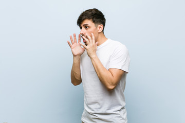 Young caucasian man wearing a white tshirt shouts loud, keeps eyes opened and hands tense.