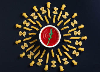 Different kind of pasta arrange on the table around pot with tomato sauce. Geometric pattern of pasta. Italian pasta with tomato sauce.