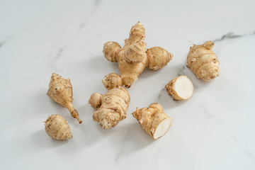 Root of topinabour on a white marble background. Jerusalem artichokes called sunroot.