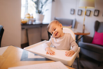 Portrait of adorable little girl on highchair. Baby laughing and play. Happy girl smile