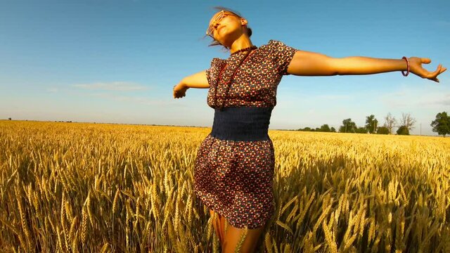girl in short dress exposes face and hands to sun among yellow wheaten field blue sky