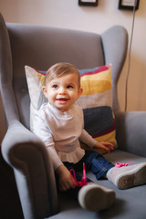 Cute baby girl sitting on big armchair and smile