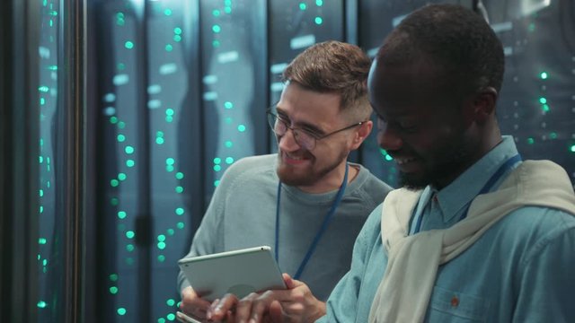 Friendly mixed-race server engineers talking fun things and jokes laughing together while coworking in digital server room at data center.